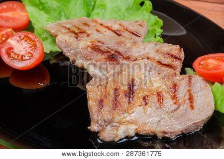 Grilled Sappy Pork Neck Steaks With Lettuce Leaves And Cherry Tomatoes On Black Dish Close-up At Sel