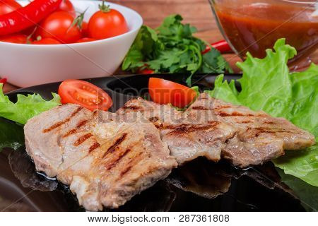 Grilled Sappy Pork Neck Steaks With Lettuce Leaves And Cherry Tomatoes On Black Dish Against Of Vege