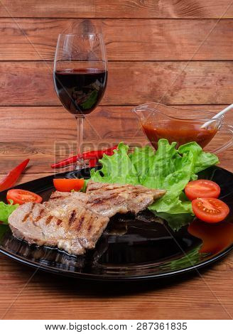 Grilled Sappy Pork Neck Steaks With Lettuce Leaves And Cherry Tomatoes On Black Dish, Glass Of Red W