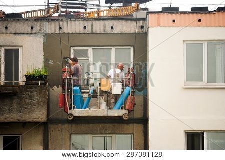 Two Workers Are Plastering The Facade Of A Building Without Observing Safety Techniques In A Cradle 