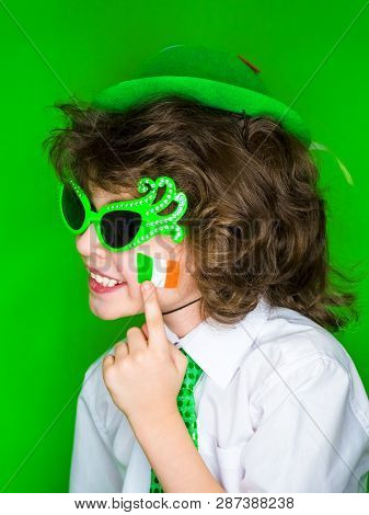 Child Celebrating St. Patricks Day Showing His Make-up. A Small, Curly Boy In Green Carnival Accesso