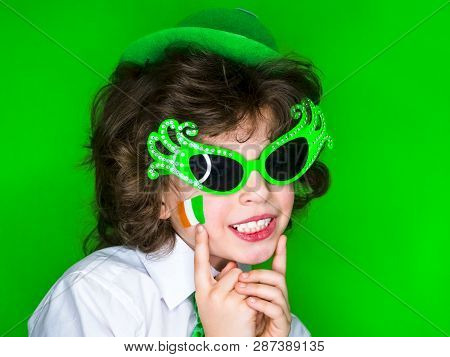 Child Celebrating St. Patricks Day Showing His Make-up. A Small, Curly Boy In Green Carnival Accesso