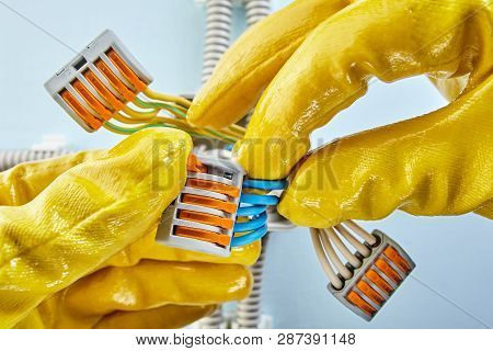 Electrician In Yellow Protective Gloves Is Connecting Three Groups Of Wires Of Plastic Junction Box.