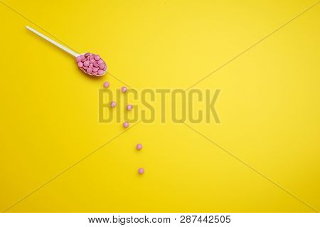 Top View Of Assorted Pharmaceutical Medicine Pink Pills, Tablets On Plastic Spoon On Yellow Backgrou