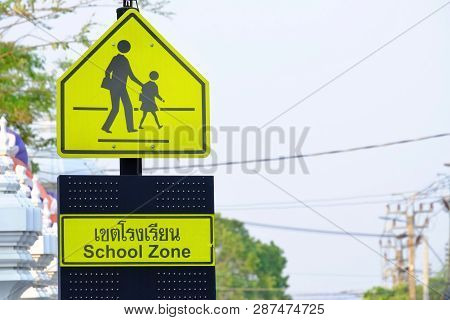 A Yellow Signboard Of School Zone On Black High Pole Beside The Road With White Sky Background (a Th