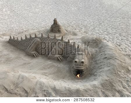 A Sand Sculpture In The Shape Of A Dragon That Exhales Fire From The Mouth Located On The Beach
