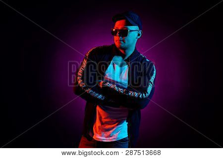 Portrait Of A Young Happy Serious Man In Cap, White Shirt, Bomber And Sunglasses At Studio. High Fas