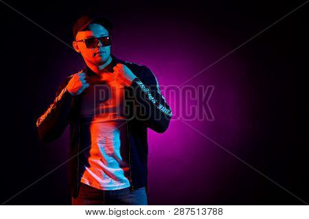 Portrait Of A Young Happy Serious Man In Cap, White Shirt, Bomber And Sunglasses At Studio. High Fas