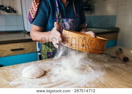 Grandmother Cooking, Hands Of Old Woman Sifting Flour Through A Sieve Onto Dough.