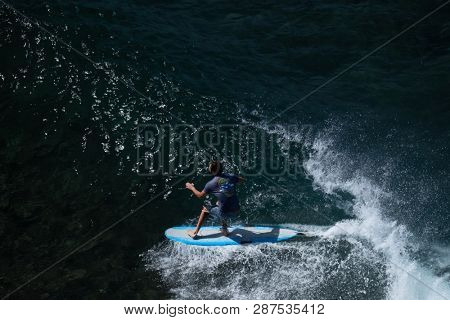 MAUI / USA - 14 DECEMBER 2018: Young longboard surfer tries to do nose riding trick while glides on the wave at Honolua surf spot on the north of Maui, Hawaii