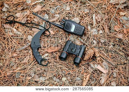 Binoculars, Radio Set And Karambit Knife On The Ground Covered With Pine Needles
