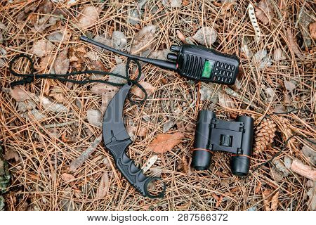 Binoculars, Radio Set And Karambit Knife On The Ground Covered With Pine Needles