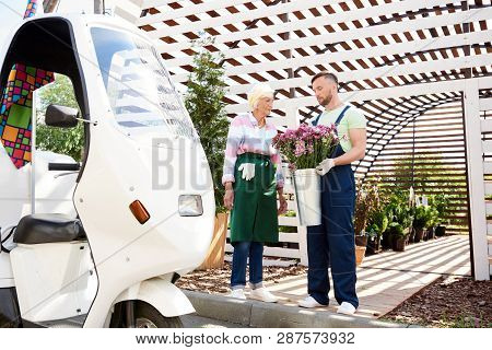 Full Length Portrait Of Two Gardeners Preparing Flowers For Delivery Standing By Beautiful Plantatio