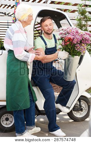 Full Length Portrait Of Smiling Handsome Man Delivering Flowers Sitting In Car On Plantation Lit By 