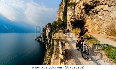 Cycling woman riding on bike at sunrise mountains and Garda lake landscape. Cycling MTB enduro flow sentiero ponale trail track. Outdoor sport activity.