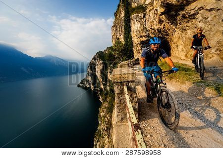 Cycling woman and man riding on bikes at sunrise mountains and Garda lake landscape. Couple cycling MTB enduro flow sentiero ponale trail track. Outdoor sport activity.