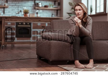 Blonde-haired Depressed Woman Sitting On Sofa And Thinking