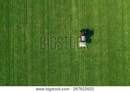Agricultural Tractor Is Fertlizing Wheat Crop Field With Npk Fertilizers, Aerial View From Drone Pov