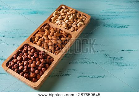 Compartmental Dish With Nuts On Blue Wooden Table. Cashew, Hazelnut, Almond.