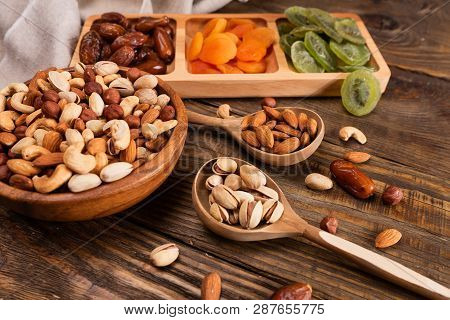 Dates, Dried Apricots And Kiwis In A Compartmental Dish And Assortment Of Nuts In Wooden Bowl On A D