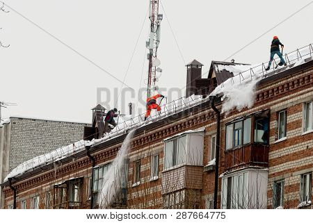 Tyumen, Russia - February 19, 2019: Men With Snow Shovels Clean Residential Building Roof In Winter 