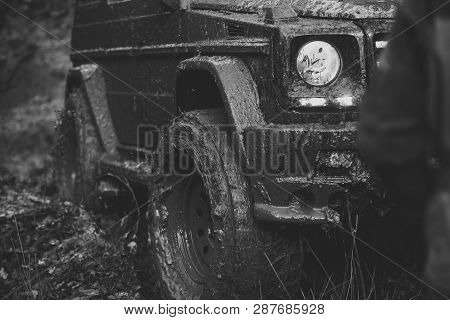 Dirty Offroad Tire Covered With Mud, Close Up. Part Of Car Stuck In Dirt And Light Turned On, Defocu
