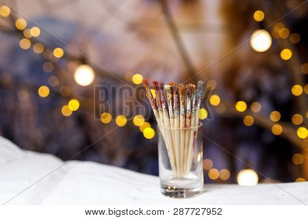 Paint Brushes In A Glass Jar With Remnants Of Paint.