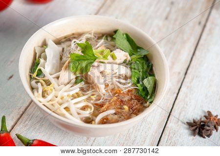 Asian rice noodles soup with vegetables and chicken in bowl on wooden background.