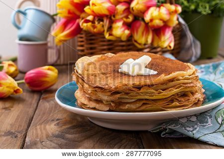 Lots Of Thin Pancakes On A Wooden Background Or Table, And A Basket With Fresh Red-yellow Tulips. Ba