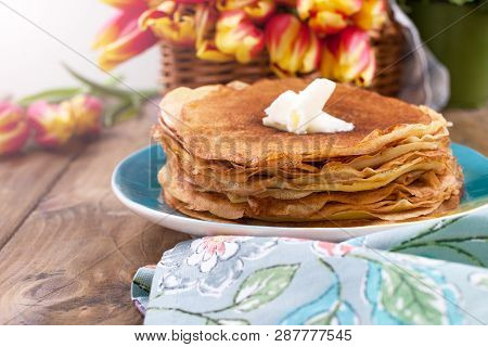 Lots Of Thin Pancakes On A Wooden Background Or Table, And A Basket With Fresh Red-yellow Tulips. Ba