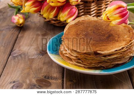 Lots Of Thin Pancakes On A Wooden Background Or Table, And A Basket With Fresh Red-yellow Tulips. Ba