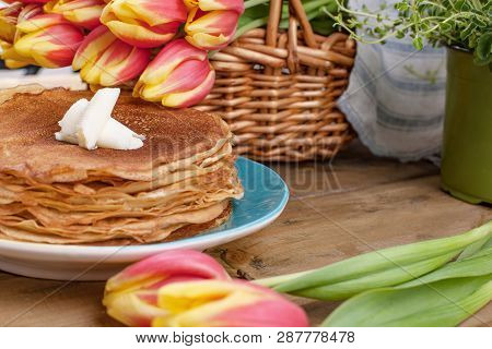 Lots Of Thin Pancakes On A Wooden Background Or Table, And A Basket With Fresh Red-yellow Tulips. Ba