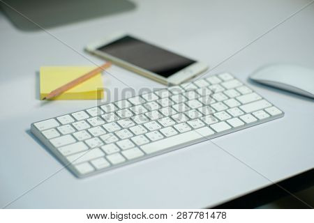 Selective Focus On White Keyborad On The Desk With Defocused Stationary, Mouse, And Mobile Phone In