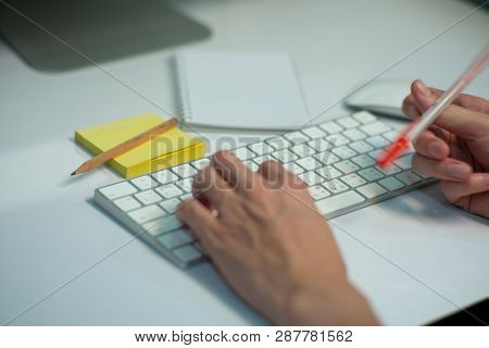 Selective Focus On White Keyboard Of Desk Top With Blurred Motion Of Hands Spinning The Pencil In Fo