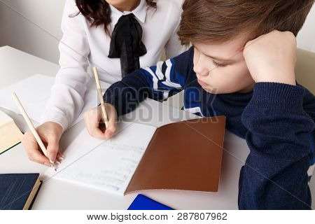 Mother And Her Son Doing Homework In The White Room. Whriting Homework In A Note.