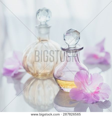 Spa Still Life With Perfume And Aromatic Oils Bottles Surrounded By Flowers, On Light Background