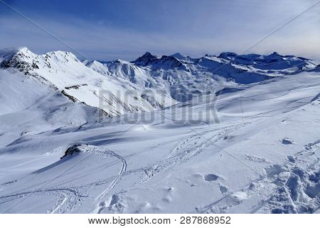 Snowy Ski Slope With Print From Skis, Snowboards And Foot, Snow Mountains And Blue Sky With Clouds