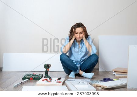 One Frustrated Woman In Blue Shirt With Tools And Furniture Items Sits On The Floor. Difficulties Of