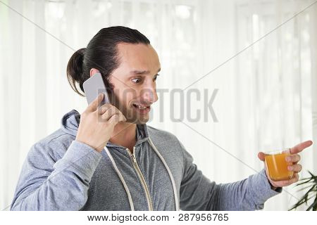 Scared Emotional Young Man Talking On Phone And Looking On Glass Of Juice In His Hand