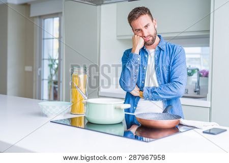 Handsome man cooking italian spaghetti pasta at the kitchen thinking looking tired and bored with depression problems with crossed arms.
