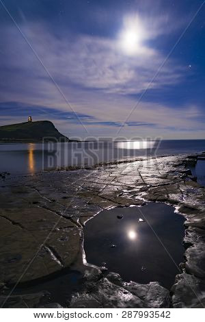 The Moon Illuminates Becalmed Seas In Kimmeridge Ledges With Clavell Tower Lights Reflected In The B