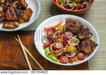 Plates Of Pan-asian Sesame Salad And Grilled Chicken Pieces In Terriyaki Sauce.
