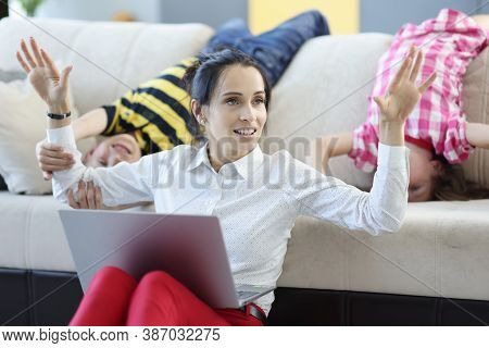 Woman Is Sitting On Floor With Laptop Raising Her Hands Up Behind Her Children Are Indulging. Remote