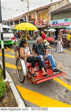 George Town, Penang, Malaysia - December 1, 2019: Classic Local Rickshaw With Tourists In Cloudy Wea