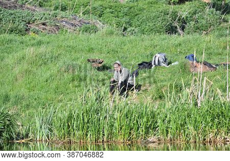 Woman Sitting On The Watersand Of The Pond Catching Fish