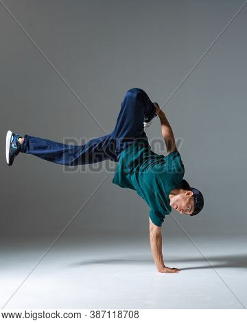 Cool Guy Breakdancer Dance On The Floor Standing On One Hand Isolated On Gray Background. Breakdance