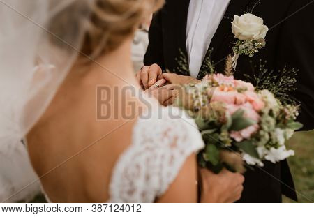 The Groom Is Putting The Wedding Ring On The Bride. Image Has Been Taken Over The Shoulder Of A Brid