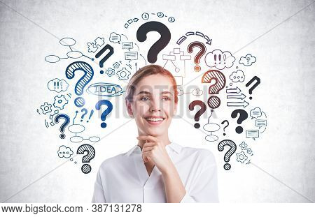Cheerful Young Businesswoman Standing Near Concrete Wall With Question Marks And Business Icons Draw