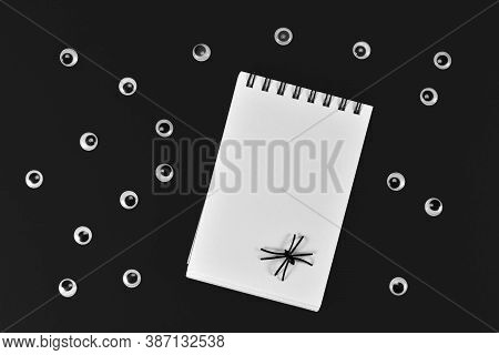 Halloween Flat Lay With Lots Of Googly Eyes And Empty Notepad With Spider On Black Background