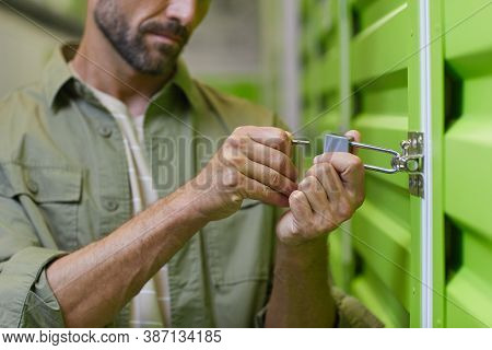 Close Up Of Handsome Man Opening Padlock On Door Of Self Storage Unit , Copy Space